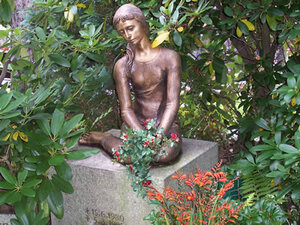 Mädchenfigur sitzend auf einem Grabstein.